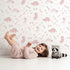 Lovely child standing in front of Whimsy Tots Dino Fossil Footprints Wallpaper in Dusty Pink with dinosaur, fossil, bone, footprint in design. Lovely child standing in front of Whimsy Tots Dino Fossil Footprints Wallpaper in Dusty Pink with dinosaur, fossil, bone, footprint in design.