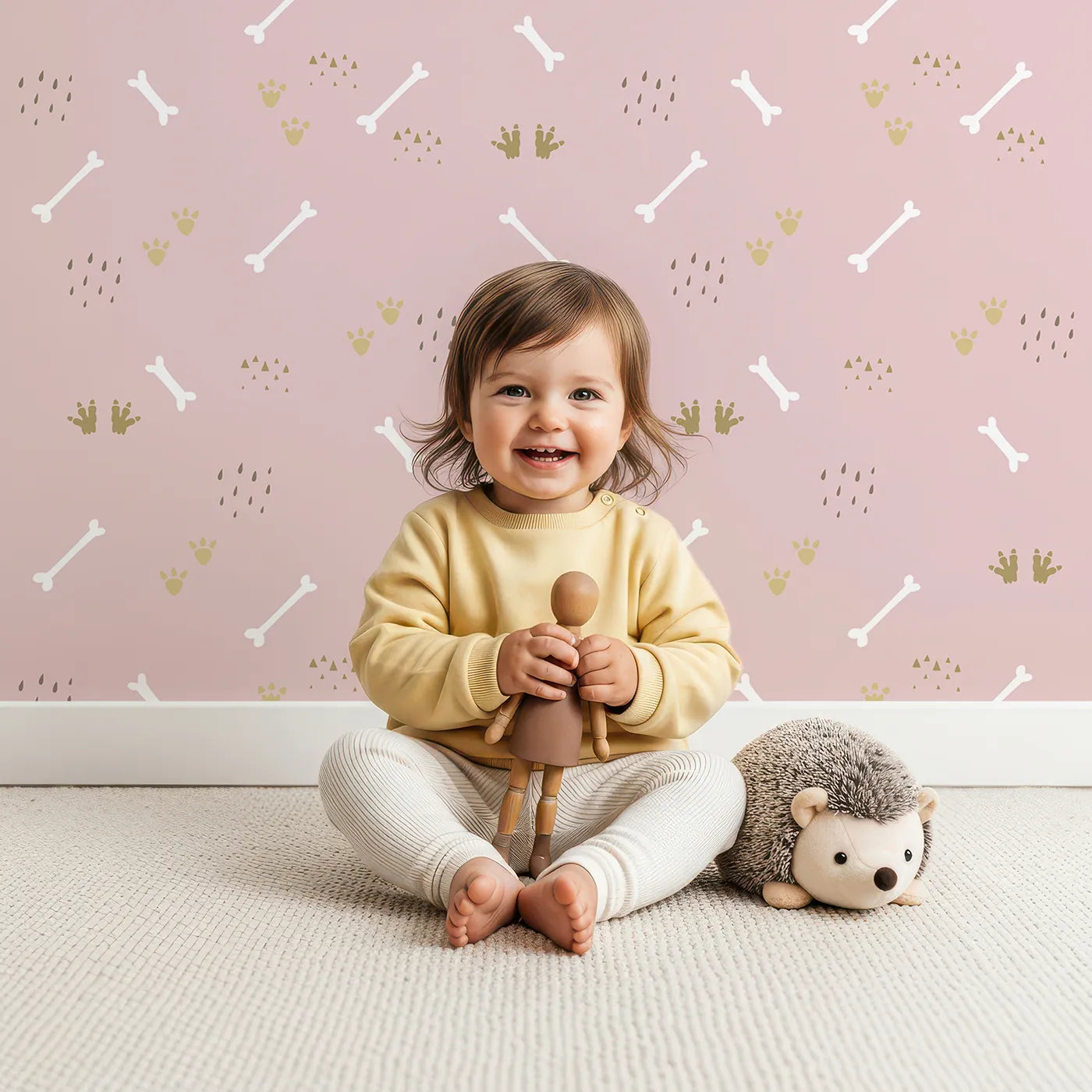 Lovely child standing in front of Whimsy Tots Dino Dig Basics Wallpaper in Rose Blush Pink with bone, footprint, raindrop, track in design.