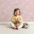 Lovely child standing in front of Whimsy Tots Dino Dig Basics Wallpaper in Rose Blush Pink with bone, footprint, raindrop, track in design. Lovely child standing in front of Whimsy Tots Dino Dig Basics Wallpaper in Rose Blush Pink with bone, footprint, raindrop, track in design.