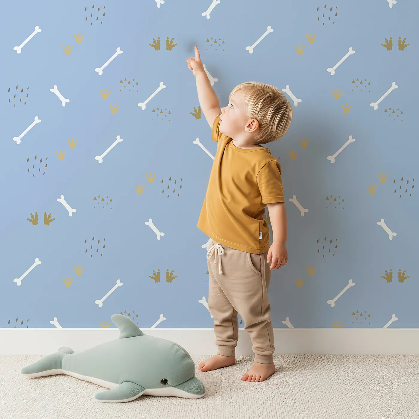 Lovely child standing in front of Whimsy Tots Dino Dig Basics Wallpaper in Dusk Blue with bone, footprint, raindrop, track in design.