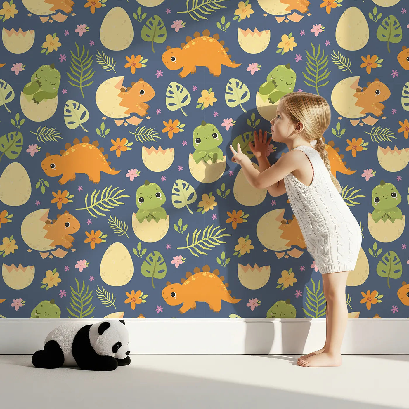 Lovely child standing in front of Whimsy Tots Hatchling Dino Garden Wallpaper in Midnight Nest with dinosaur, egg, flower, leaf in design.