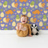 Lovely child standing in front of Whimsy Tots Hatchling Dino Garden Wallpaper in Blossom Lilac Lavender with dinosaur, egg, flower, leaf in design. Lovely child standing in front of Whimsy Tots Hatchling Dino Garden Wallpaper in Blossom Lilac Lavender with dinosaur, egg, flower, leaf in design.