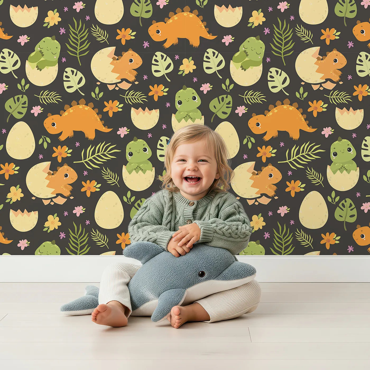 Lovely child standing in front of Whimsy Tots Hatchling Dino Garden Wallpaper in Charcoal Nest Gray with dinosaur, egg, flower, leaf in design.