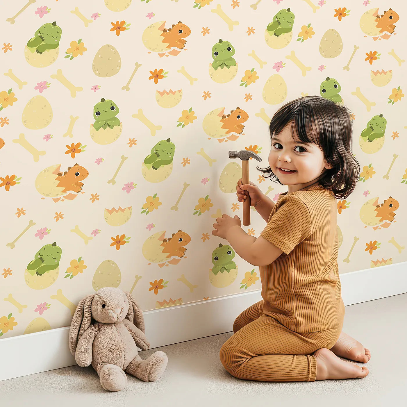 Lovely child standing in front of Whimsy Tots Hatchling Dino Parade Wallpaper in Dappled Beige with dinosaur, egg, bone, flower in design.