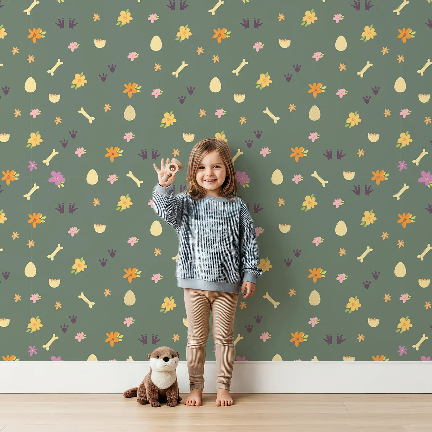 Lovely child standing in front of Whimsy Tots Dino Hatch Trail Wallpaper in Forest Fern Green with egg, bone, flower, footprint in design.