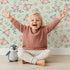 Lovely child standing in front of Whimsy Tots Whispering Peony Garden Wallpaper in Mint Petal Green with flower, peony, daisy, leaf in design. Lovely child standing in front of Whimsy Tots Whispering Peony Garden Wallpaper in Mint Petal Green with flower, peony, daisy, leaf in design.