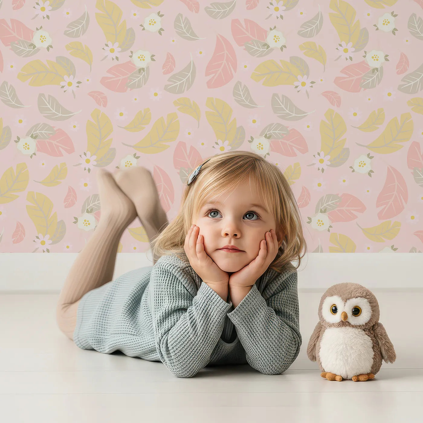 Lovely child standing in front of Whimsy Tots Floral Feather Drift Wallpaper in Blush Bloom Pink with feather, flower, blossom, leaf in design.