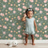 Lovely child standing in front of Whimsy Tots Twilight Garden Whimsy Wallpaper in Moss Bloom with flower, leaf, star, bloom in design. Lovely child standing in front of Whimsy Tots Twilight Garden Whimsy Wallpaper in Moss Bloom with flower, leaf, star, bloom in design.