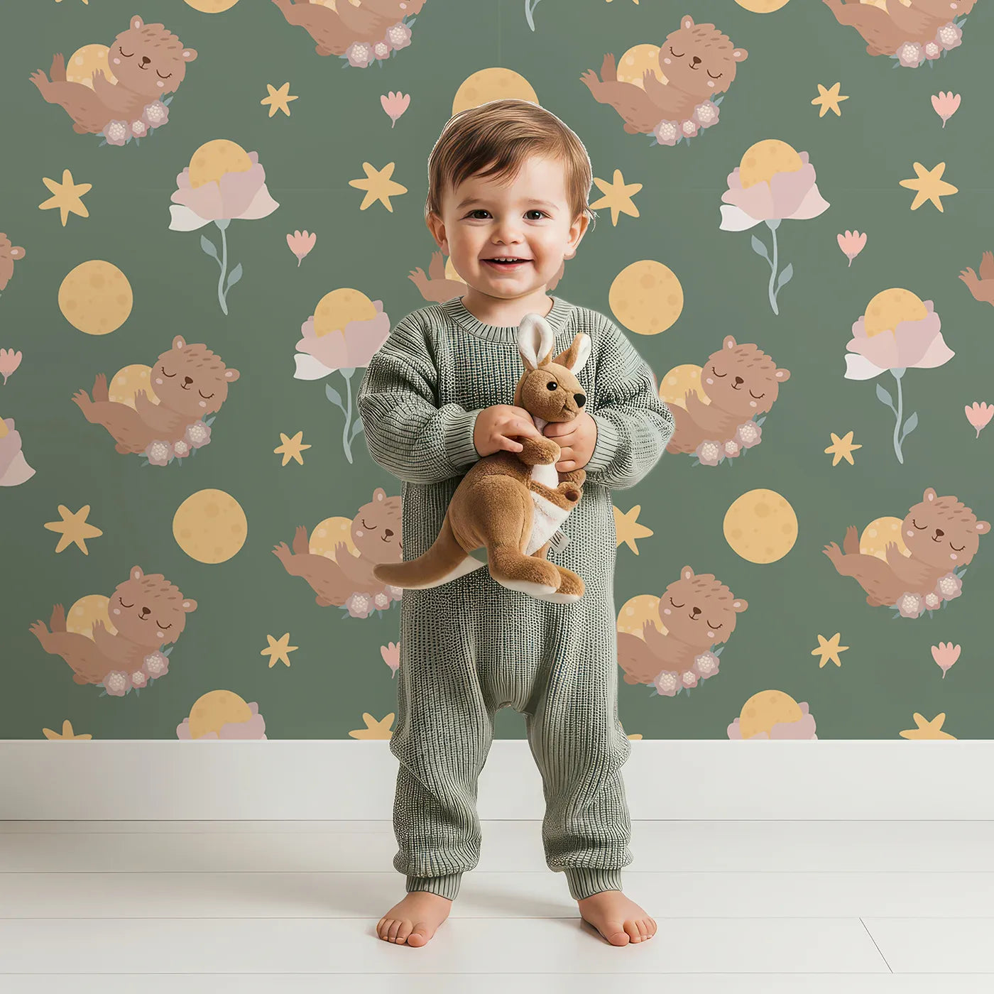 Lovely child standing in front of Whimsy Tots Moonlit Bear Dreams Wallpaper in Forest Lullaby Green with bear, flower, moon, star in design.