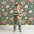 Lovely child standing in front of Whimsy Tots Moonlit Bear Dreams Wallpaper in Forest Lullaby Green with bear, flower, moon, star in design. Lovely child standing in front of Whimsy Tots Moonlit Bear Dreams Wallpaper in Forest Lullaby Green with bear, flower, moon, star in design.