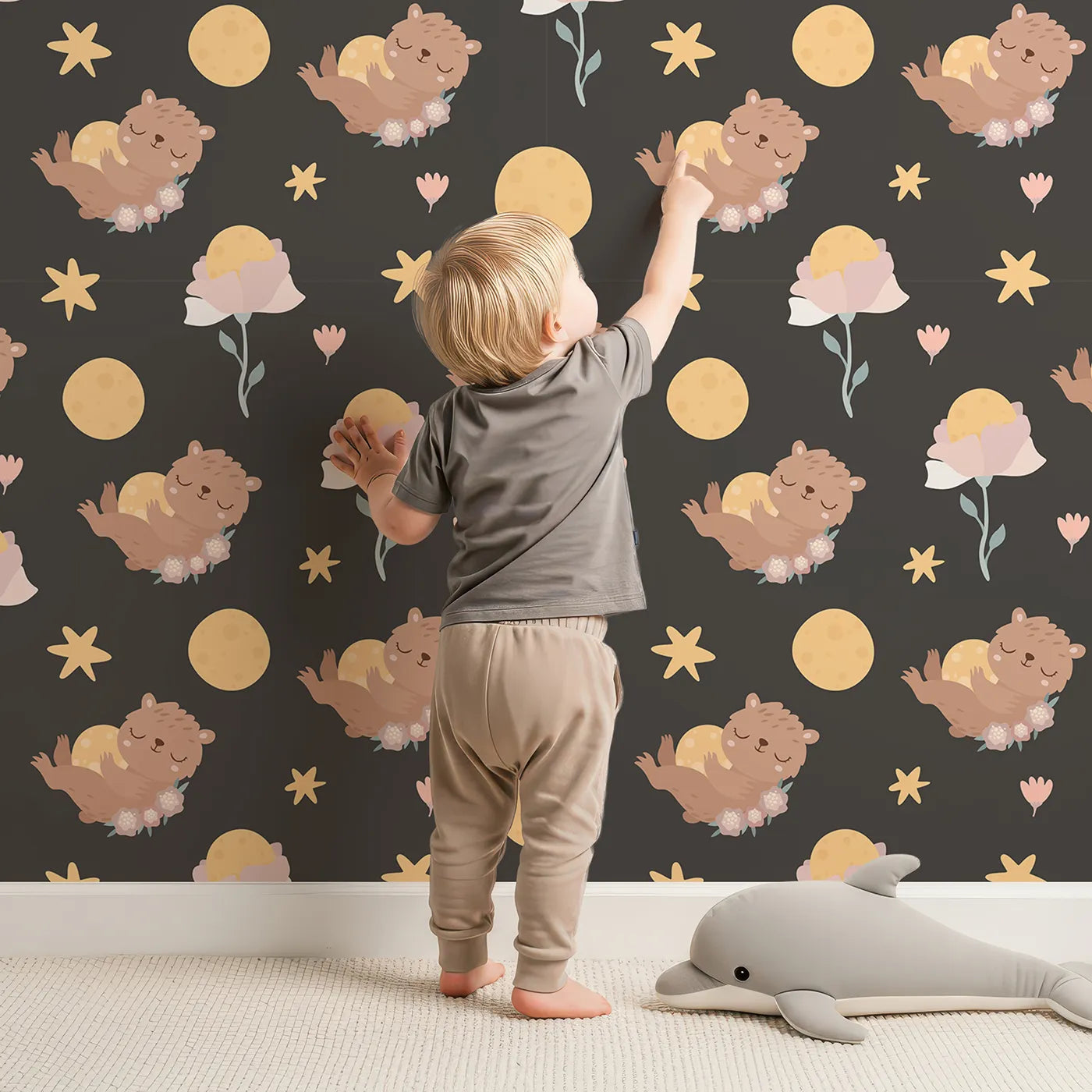 Lovely child standing in front of Whimsy Tots Moonlit Bear Dreams Wallpaper in Midnight Cocoa Brown with bear, flower, moon, star in design.