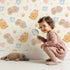 Lovely child standing in front of Whimsy Tots Royal Woodland Friends Wallpaper in Cream Crown with fox, rabbit, bear, flower, crown, star in design. Lovely child standing in front of Whimsy Tots Royal Woodland Friends Wallpaper in Cream Crown with fox, rabbit, bear, flower, crown, star in design.