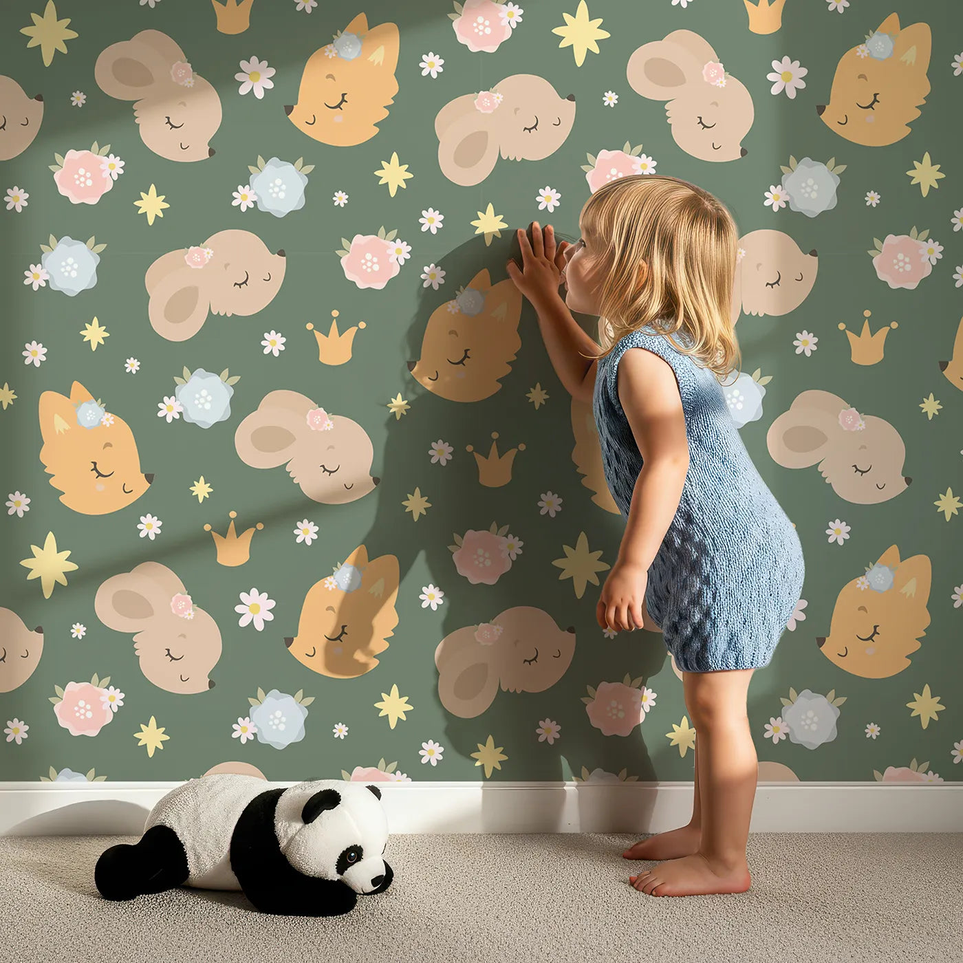 Lovely child standing in front of Whimsy Tots Royal Woodland Friends Wallpaper in Forest Crown Green with fox, rabbit, bear, flower, crown, star in design.
