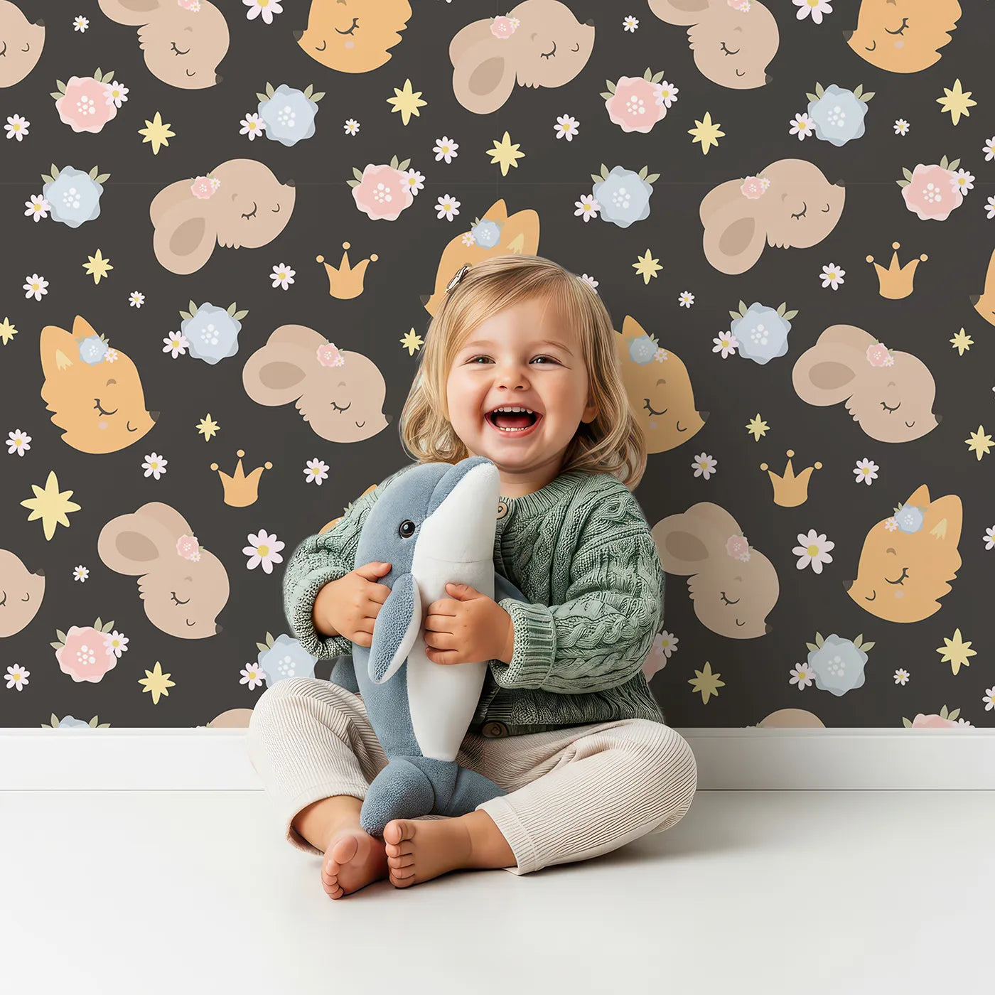 Lovely child standing in front of Whimsy Tots Royal Woodland Friends Wallpaper in Midnight Crown with fox, rabbit, bear, flower, crown, star in design.