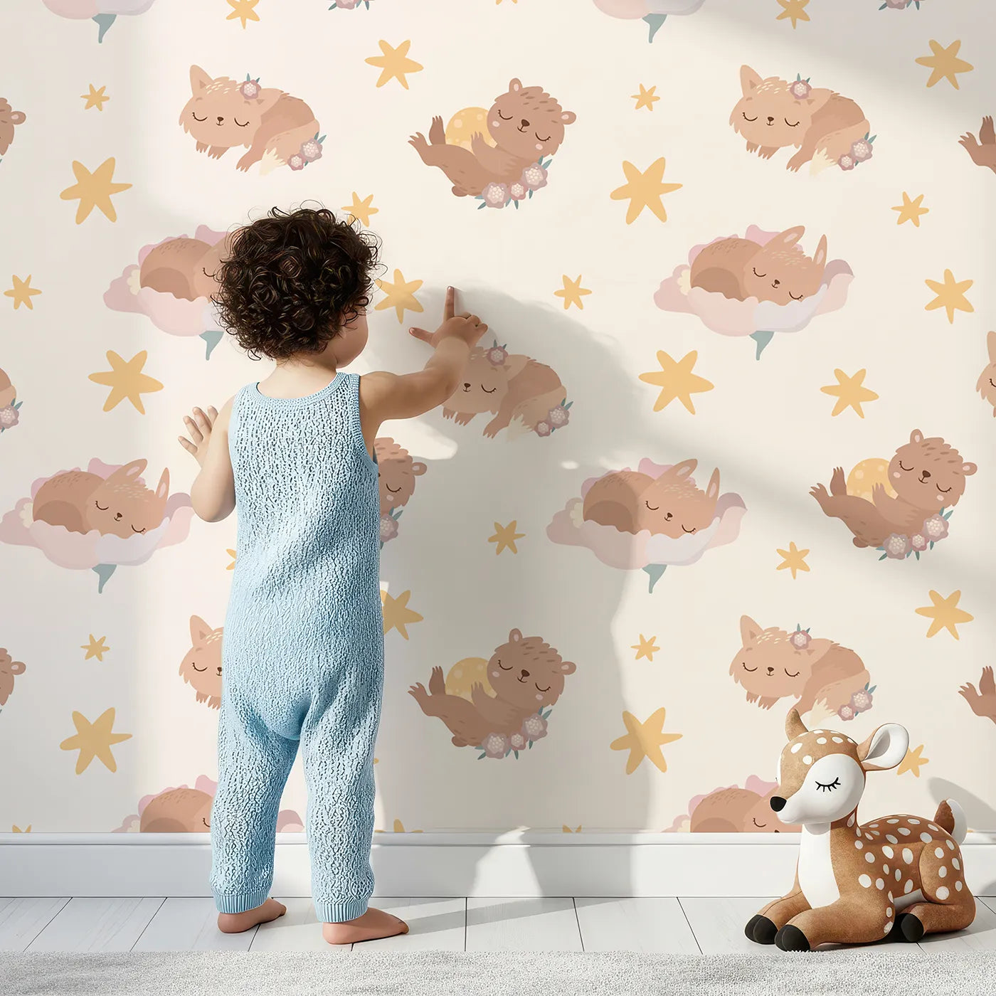 Lovely child standing in front of Whimsy Tots Woodland Nap Parade Wallpaper in Blush Pink with bear, bunny, fox, flower, star in design.