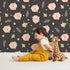 Lovely child standing in front of Whimsy Tots Blush Meadow Bloom Wallpaper in Midnight Cocoa Brown with flower, daisy, leaf, petal in design. Lovely child standing in front of Whimsy Tots Blush Meadow Bloom Wallpaper in Midnight Cocoa Brown with flower, daisy, leaf, petal in design.