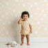 Lovely child standing in front of Whimsy Tots Gentle Pebble Dots Wallpaper in Butter Beige with dot, spot, pebble, beige in design. Lovely child standing in front of Whimsy Tots Gentle Pebble Dots Wallpaper in Butter Beige with dot, spot, pebble, beige in design.