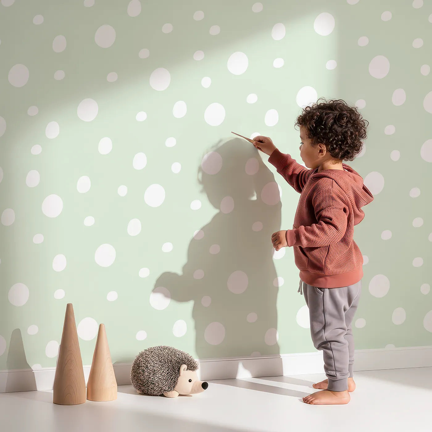 Lovely child standing in front of Whimsy Tots Gentle Pebble Dots Wallpaper in Mint Cream with dot, spot, pebble, mint in design.