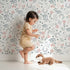 Lovely child standing in front of Whimsy Tots Wildflower Scribble Garden Wallpaper in Soft Sketch with flower, leaf, berry, stem, doodle in design. Lovely child standing in front of Whimsy Tots Wildflower Scribble Garden Wallpaper in Soft Sketch with flower, leaf, berry, stem, doodle in design.