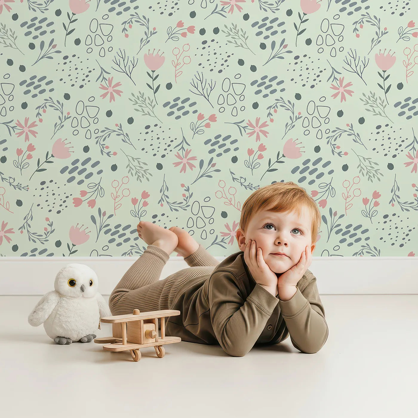 Lovely child standing in front of Whimsy Tots Wildflower Scribble Garden Wallpaper in Mint Sketch Green with flower, leaf, berry, sketch, doodle in design.