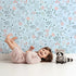 Lovely child standing in front of Whimsy Tots Wildflower Scribble Garden Wallpaper in Sky Sketch with flower, leaf, berry, sketch, doodle in design. Lovely child standing in front of Whimsy Tots Wildflower Scribble Garden Wallpaper in Sky Sketch with flower, leaf, berry, sketch, doodle in design.