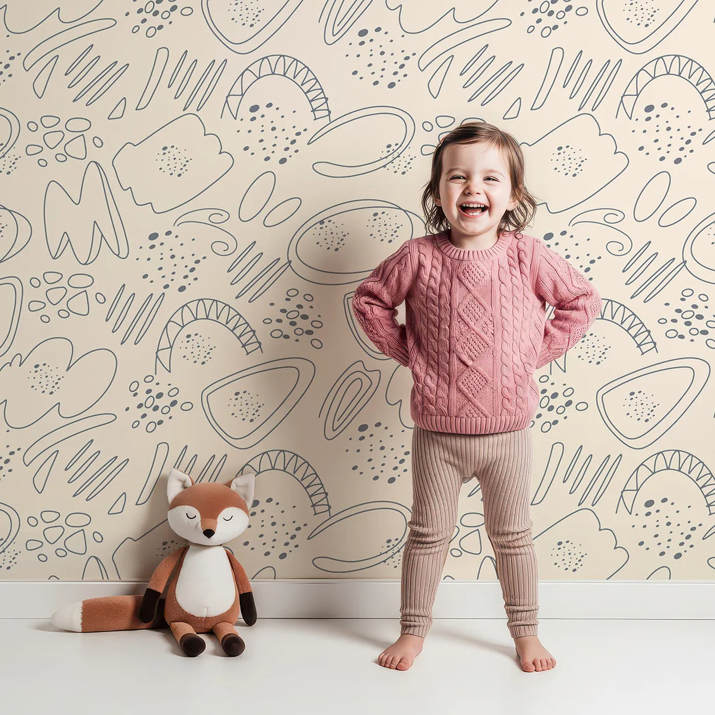 Lovely child standing in front of Whimsy Tots Doodle Meadow Shapes Wallpaper in Cream with doodle, shape, petal, scribble, arch in design.