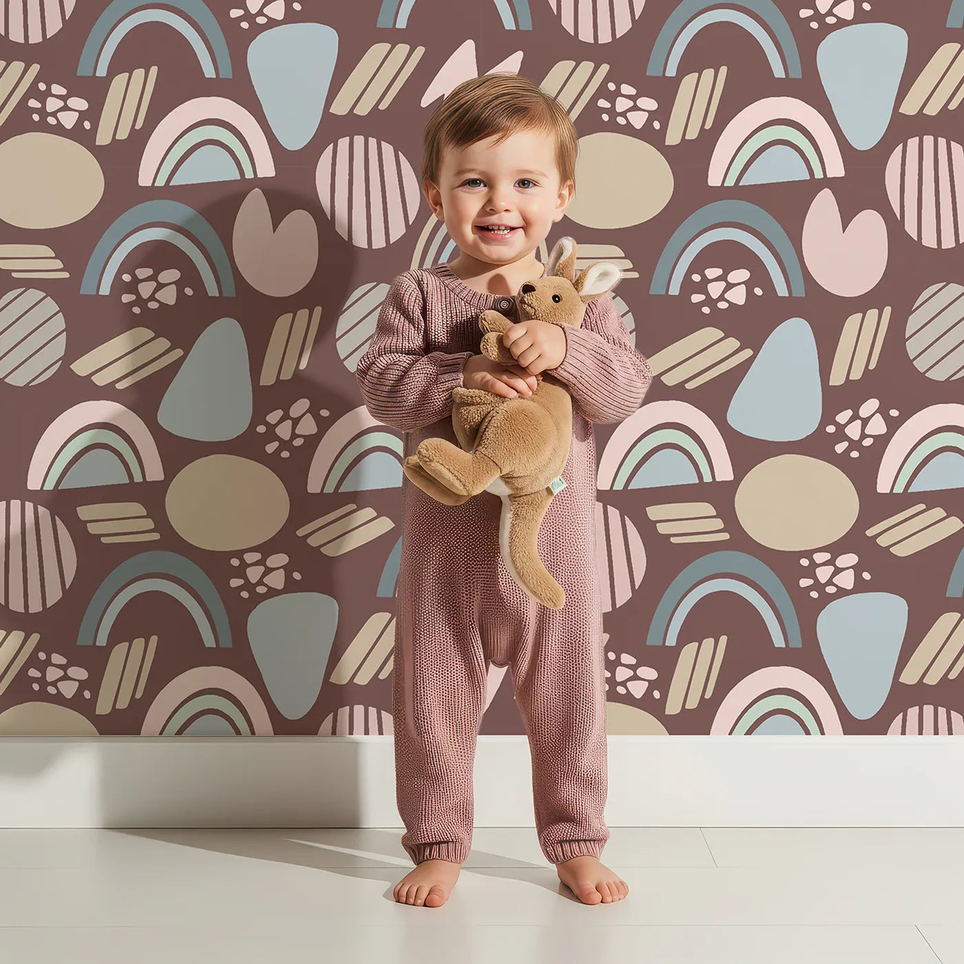 Lovely child standing in front of Whimsy Tots Rainbow Petal Shapes Wallpaper in Cocoa Brown with rainbow, petal, shape, arch, stripe in design.