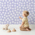 Lovely child standing in front of Whimsy Tots Playful Pebble Dots Wallpaper in Lavender Mist with dot, pebble, spot, oval in design. Lovely child standing in front of Whimsy Tots Playful Pebble Dots Wallpaper in Lavender Mist with dot, pebble, spot, oval in design.