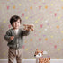 Lovely child standing in front of Whimsy Tots Cupids Arrow Parade Wallpaper in Cozy Beige with arrow, heart, star in design. Lovely child standing in front of Whimsy Tots Cupids Arrow Parade Wallpaper in Cozy Beige with arrow, heart, star in design.