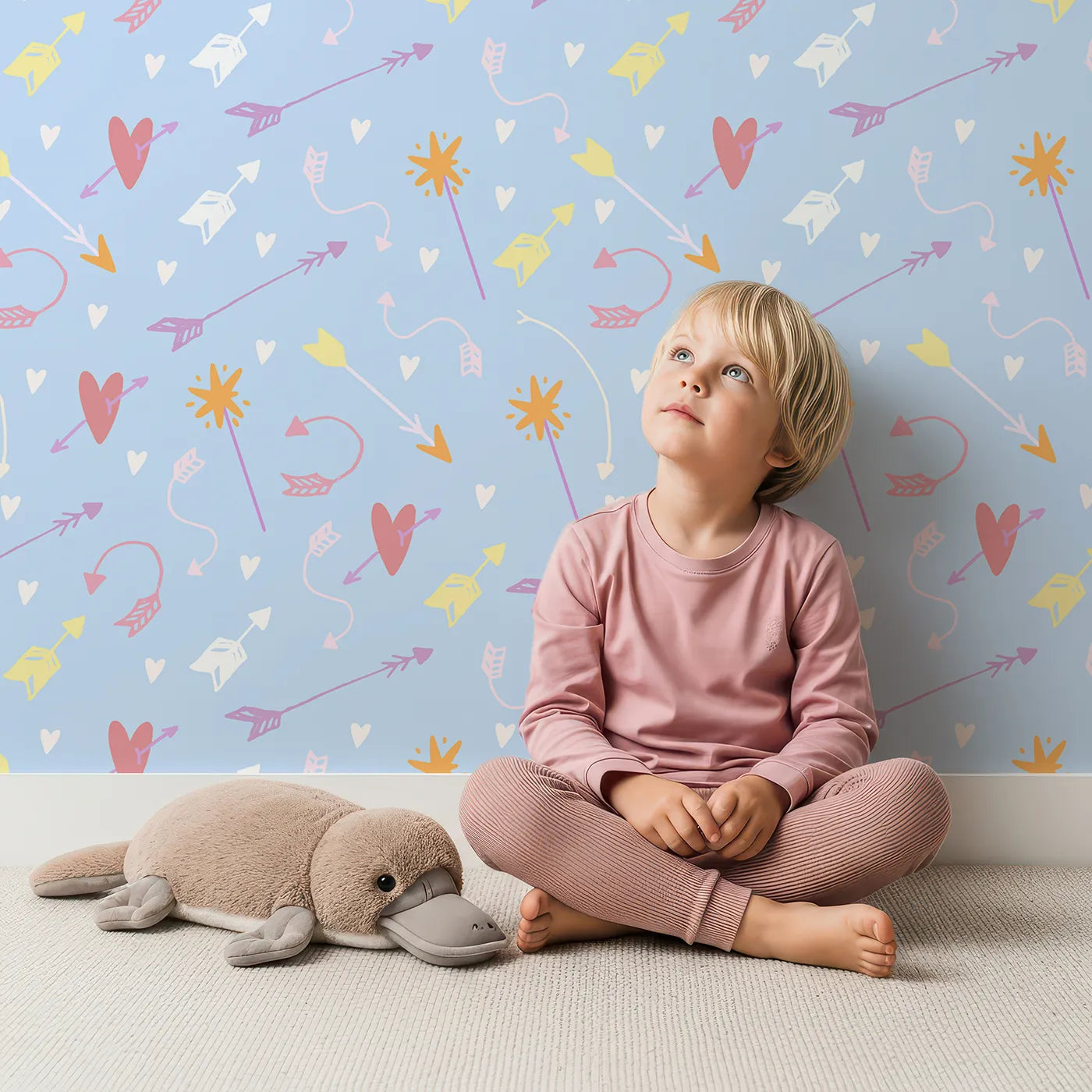Lovely child standing in front of Whimsy Tots Cupids Arrow Parade Wallpaper in Sky Blue with arrow, heart, star in design.