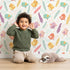 Lovely child standing in front of Whimsy Tots Feathered Joy Parade Wallpaper in Cream White with bird, feather, arrow, sprig in design. Lovely child standing in front of Whimsy Tots Feathered Joy Parade Wallpaper in Cream White with bird, feather, arrow, sprig in design.