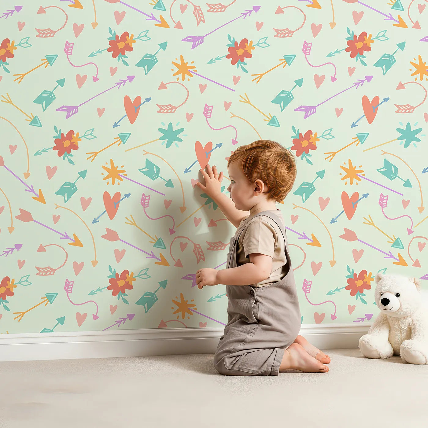 Lovely child standing in front of Whimsy Tots Love and Arrows Bloom Parade Wallpaper in Mint Green with arrow, heart, flower, burst in design.