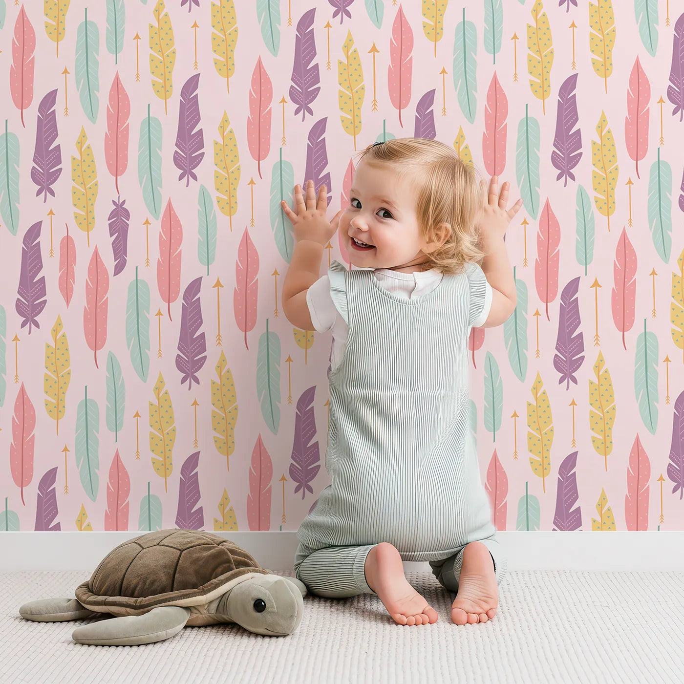Lovely child standing in front of Whimsy Tots Feather and Arrow Meadow Parade Wallpaper in Blush Pink with feather, arrow, leaf in design.