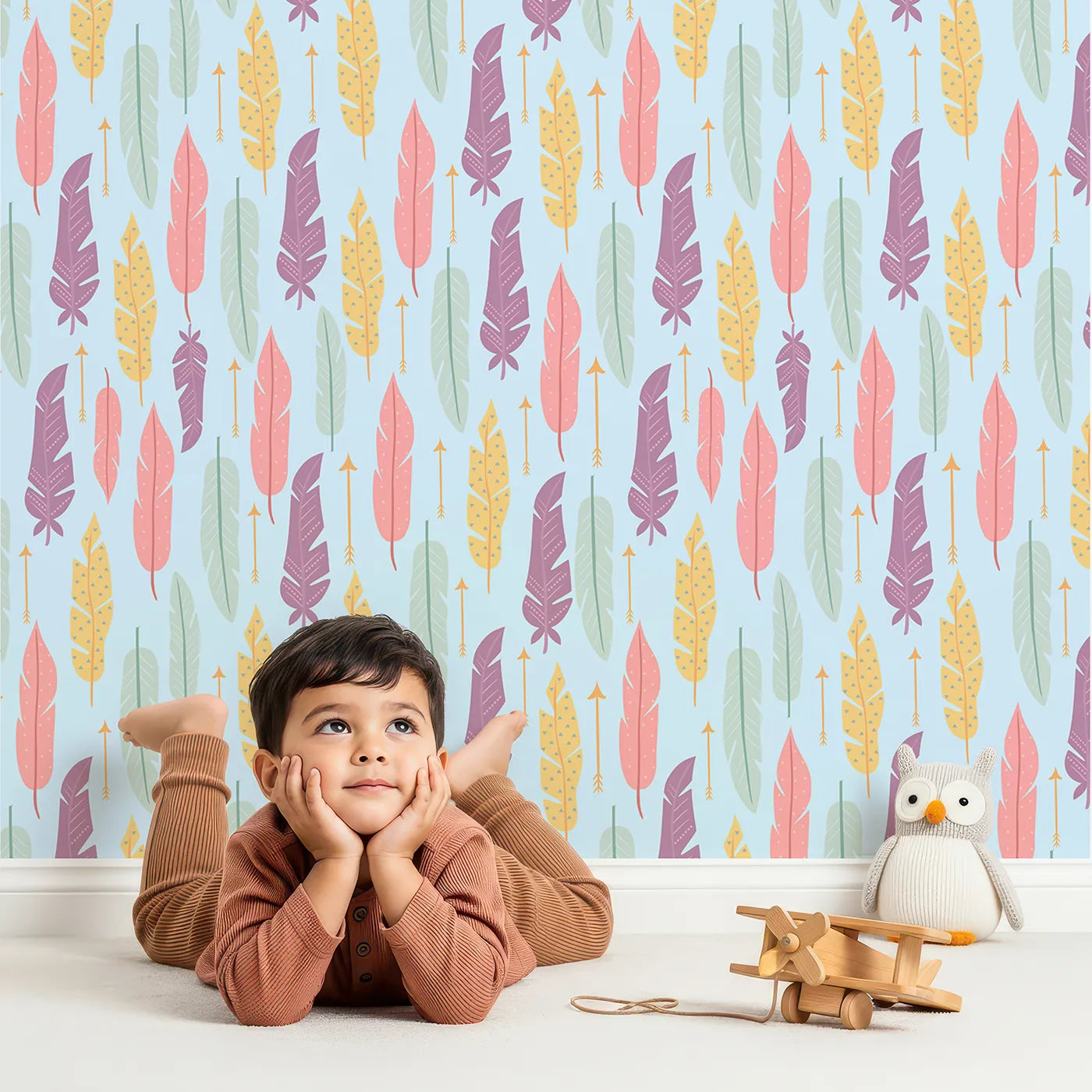 Lovely child standing in front of Whimsy Tots Feather and Arrow Meadow Parade Wallpaper in Sky Blue with feather, arrow, leaf in design.
