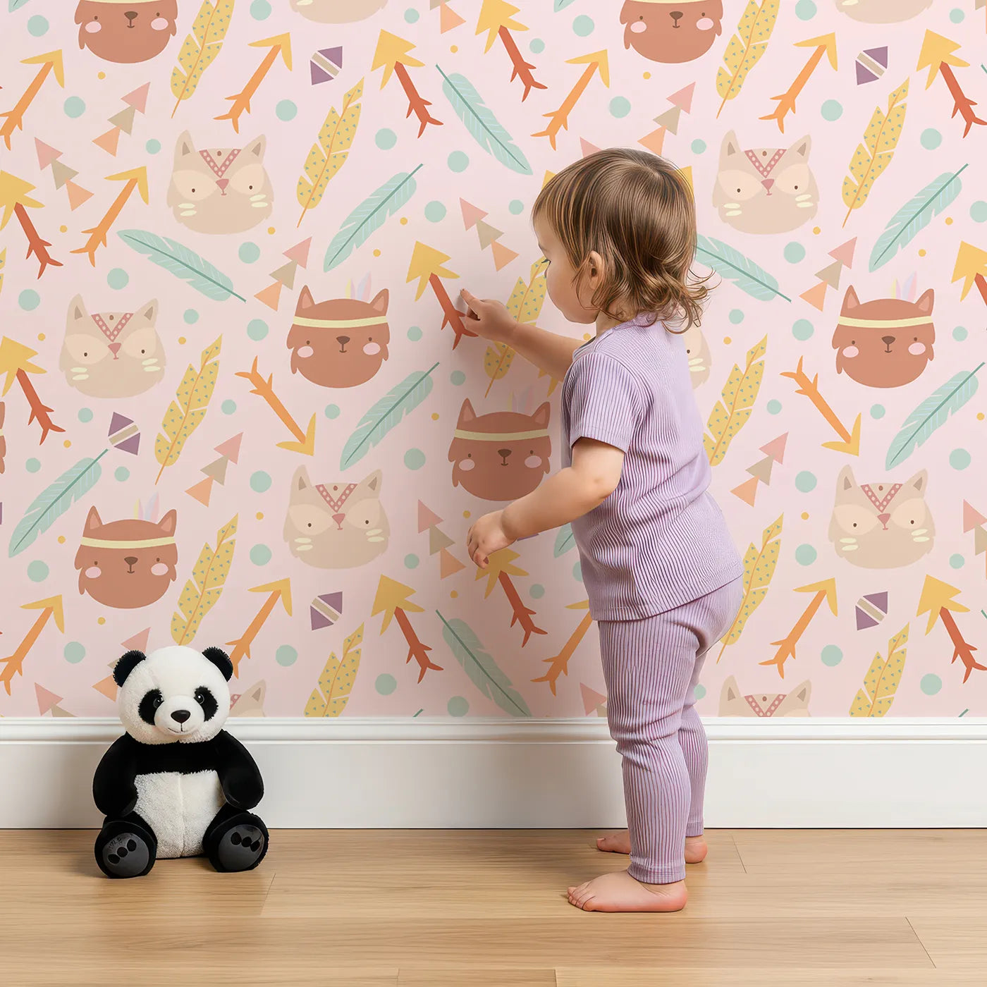 Lovely child standing in front of Whimsy Tots Tribal Kitten Parade Wallpaper in Blush Pink with cat, feather, arrow, triangle, dot in design.