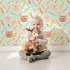 Lovely child standing in front of Whimsy Tots Tribal Kitten Parade Wallpaper in Soft Mint Green with cat, feather, arrow, triangle, dot in design. Lovely child standing in front of Whimsy Tots Tribal Kitten Parade Wallpaper in Soft Mint Green with cat, feather, arrow, triangle, dot in design.