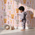 Lovely child standing in front of Whimsy Tots Mindful Kitten Heart Wallpaper in Petal Blush Pink with cat, heart, triangle, dot, diamond in design. Lovely child standing in front of Whimsy Tots Mindful Kitten Heart Wallpaper in Petal Blush Pink with cat, heart, triangle, dot, diamond in design.