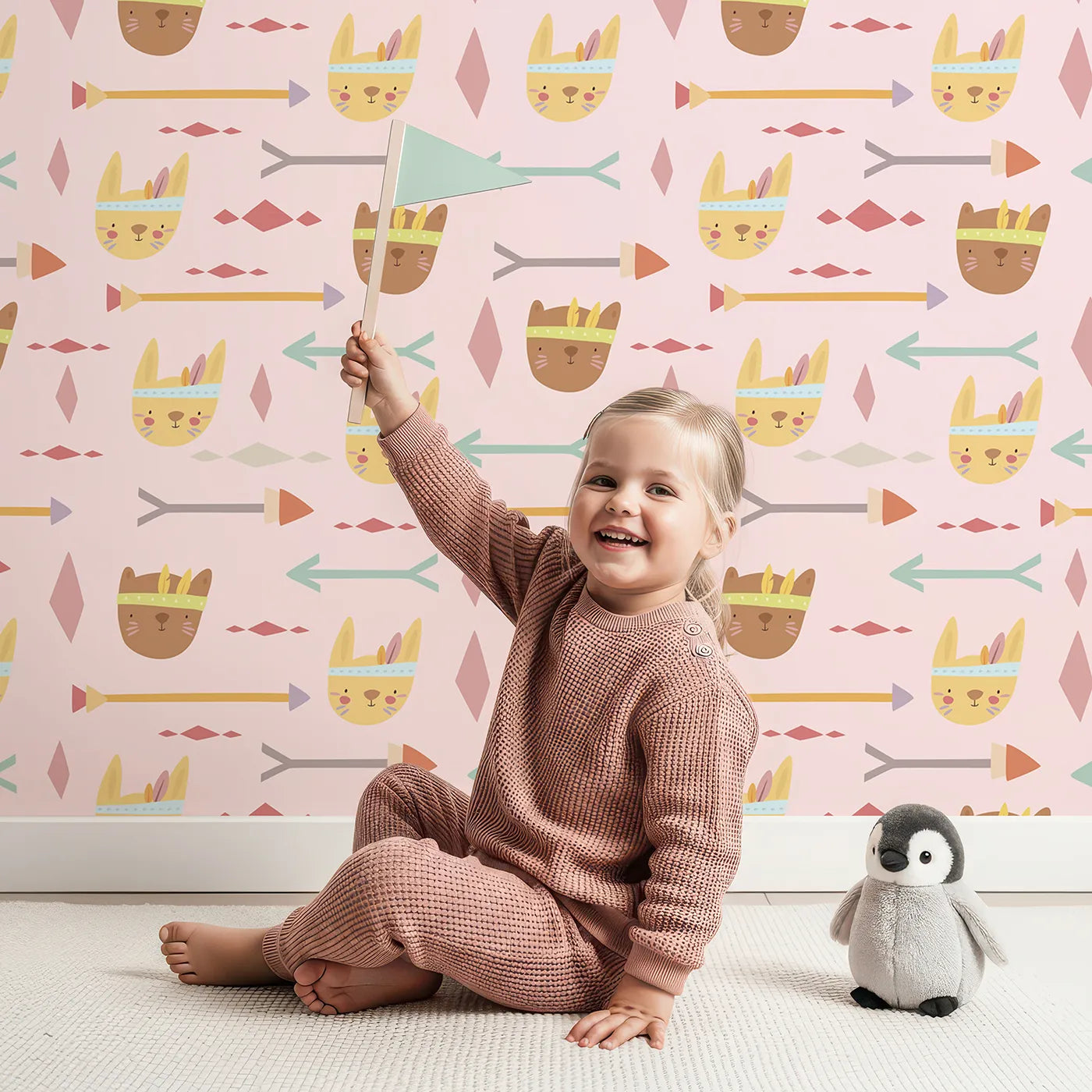Lovely child standing in front of Whimsy Tots Tribal Bunny Parade Wallpaper in Petal Blush Pink with rabbit, arrow, feather, diamond in design.
