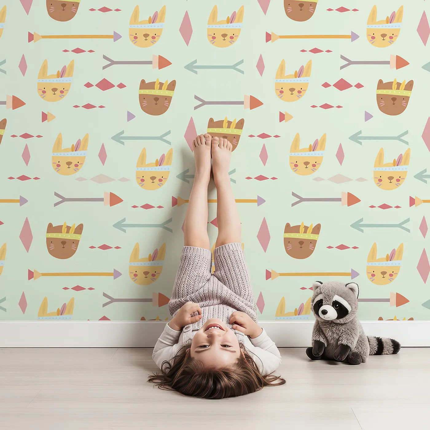 Lovely child standing in front of Whimsy Tots Tribal Bunny Parade Wallpaper in Fresh Sage Green with rabbit, arrow, feather, diamond in design.