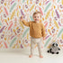 Lovely child standing in front of Whimsy Tots Feather Arrow Confetti Wallpaper in White with arrow, feather, triangle, dot in design. Lovely child standing in front of Whimsy Tots Feather Arrow Confetti Wallpaper in White with arrow, feather, triangle, dot in design.
