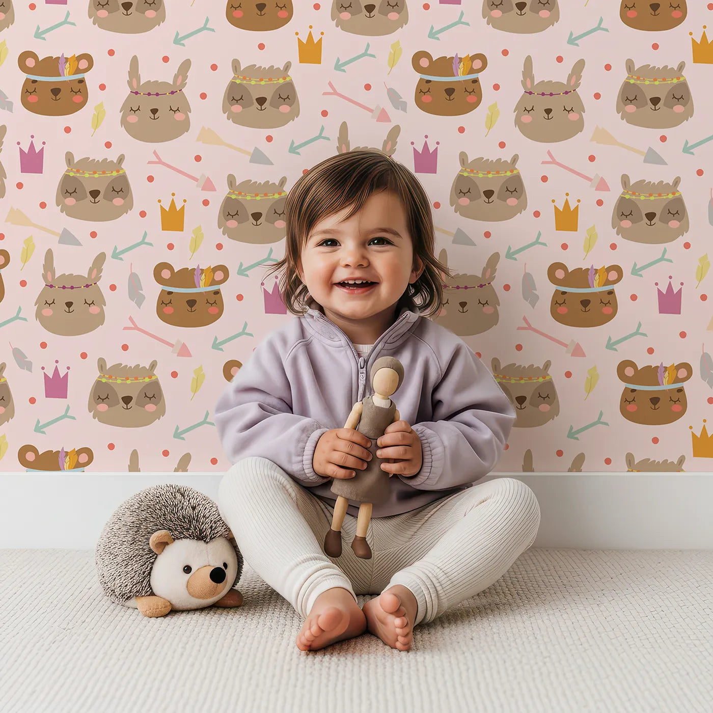 Lovely child standing in front of Whimsy Tots Feather Crown Critters Wallpaper in Petal Pink with bear, rabbit, crown, feather, arrow, dot in design.