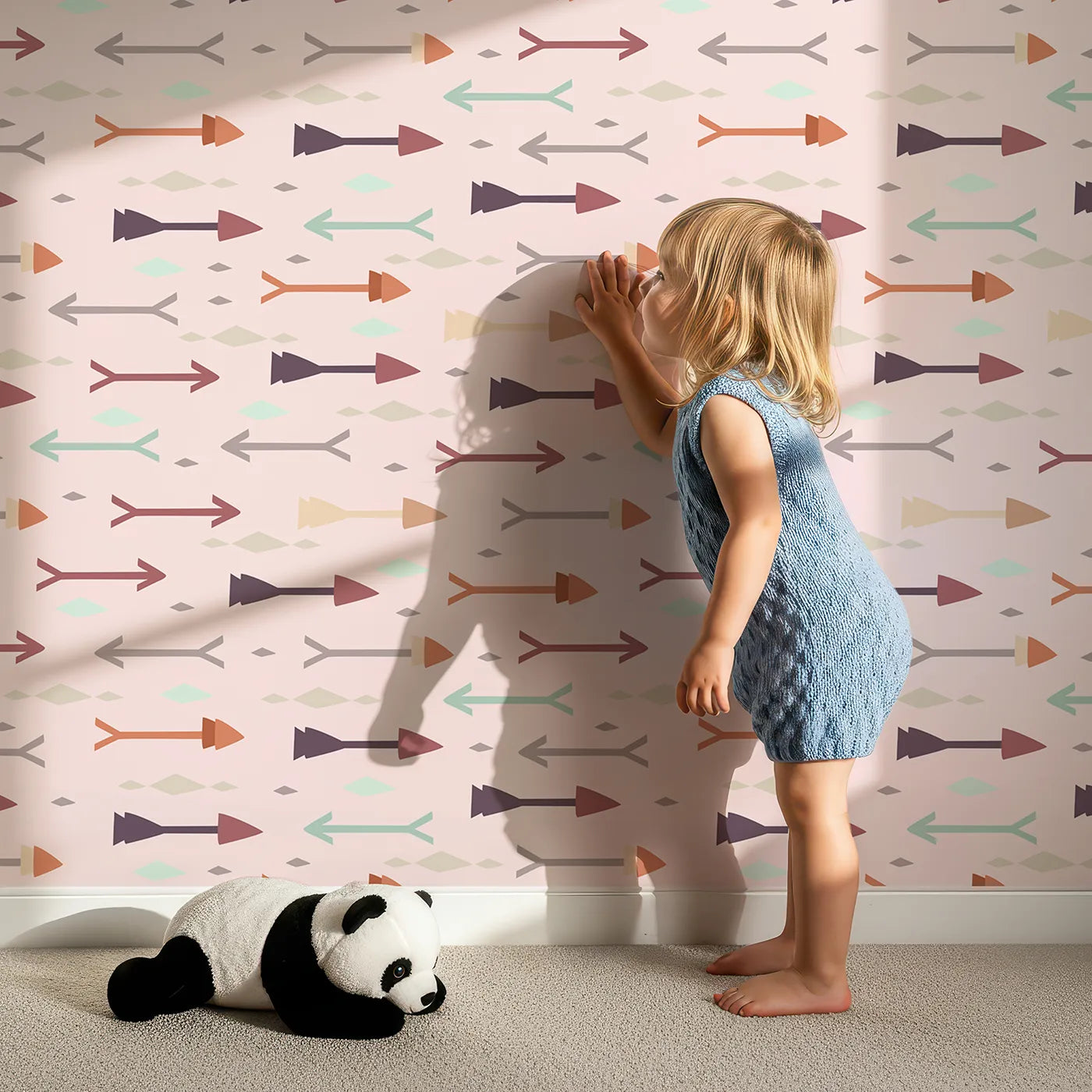 Lovely child standing in front of Whimsy Tots Boho Arrow Trail Wallpaper in Blush Pink with arrow, diamond in design.