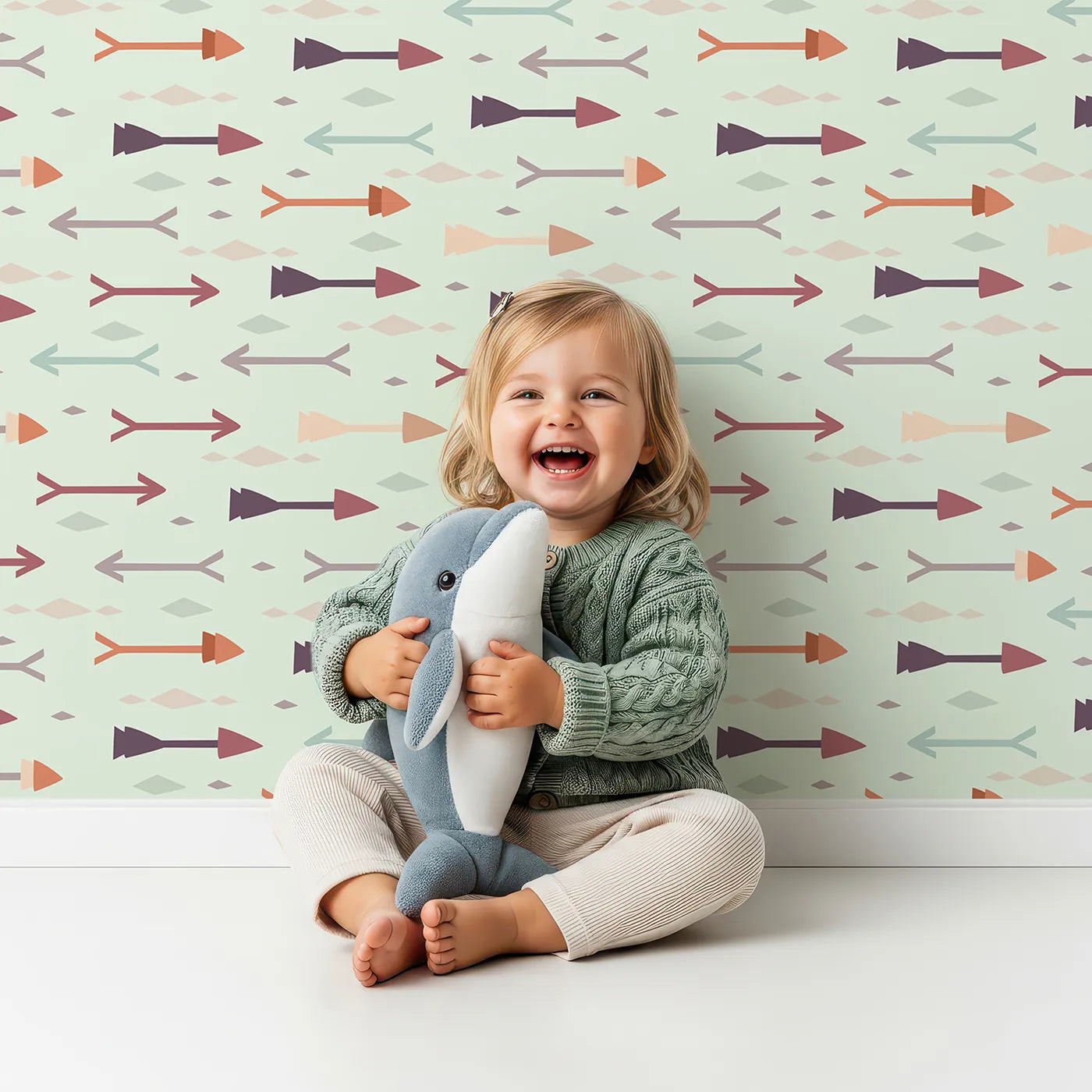 Lovely child standing in front of Whimsy Tots Boho Arrow Trail Wallpaper in Mint Green with arrow, diamond in design.
