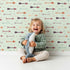 Lovely child standing in front of Whimsy Tots Boho Arrow Trail Wallpaper in Mint Green with arrow, diamond in design. Lovely child standing in front of Whimsy Tots Boho Arrow Trail Wallpaper in Mint Green with arrow, diamond in design.