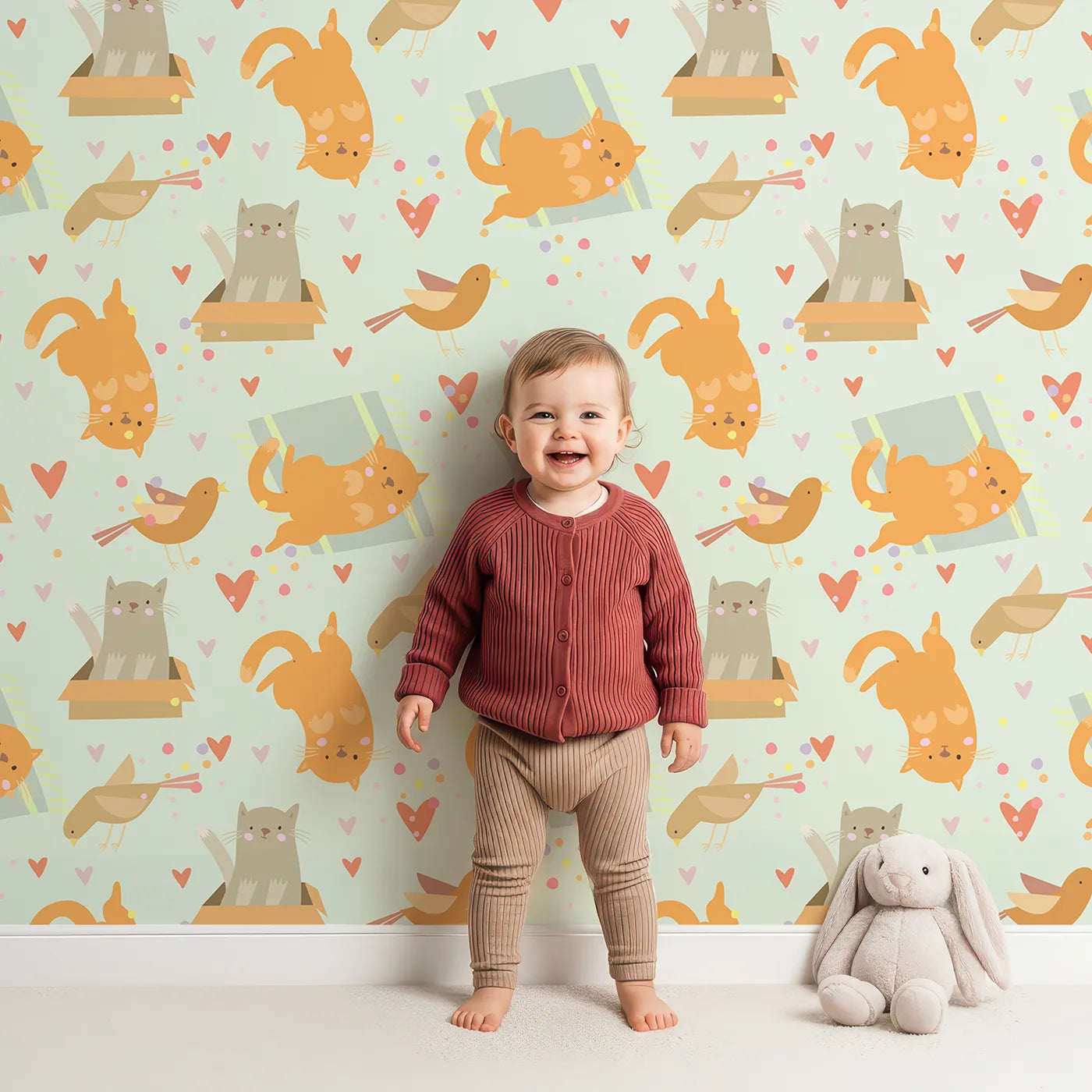 Lovely child standing in front of Whimsy Tots Catnap and Chirp Parade Wallpaper in Mint Green with cat, bird, box, heart, confetti in design.