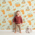 Lovely child standing in front of Whimsy Tots Catnap and Chirp Parade Wallpaper in Mint Green with cat, bird, box, heart, confetti in design. Lovely child standing in front of Whimsy Tots Catnap and Chirp Parade Wallpaper in Mint Green with cat, bird, box, heart, confetti in design.