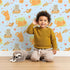 Lovely child standing in front of Whimsy Tots Catnap and Chirp Parade Wallpaper in Blue with cat, bird, box, heart, confetti in design. Lovely child standing in front of Whimsy Tots Catnap and Chirp Parade Wallpaper in Blue with cat, bird, box, heart, confetti in design.
