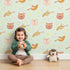 Lovely child standing in front of Whimsy Tots Feathered Friends and Fuzzy Faces Parade Wallpaper in Mint with cat, fox, bird, feather, star in design. Lovely child standing in front of Whimsy Tots Feathered Friends and Fuzzy Faces Parade Wallpaper in Mint with cat, fox, bird, feather, star in design.