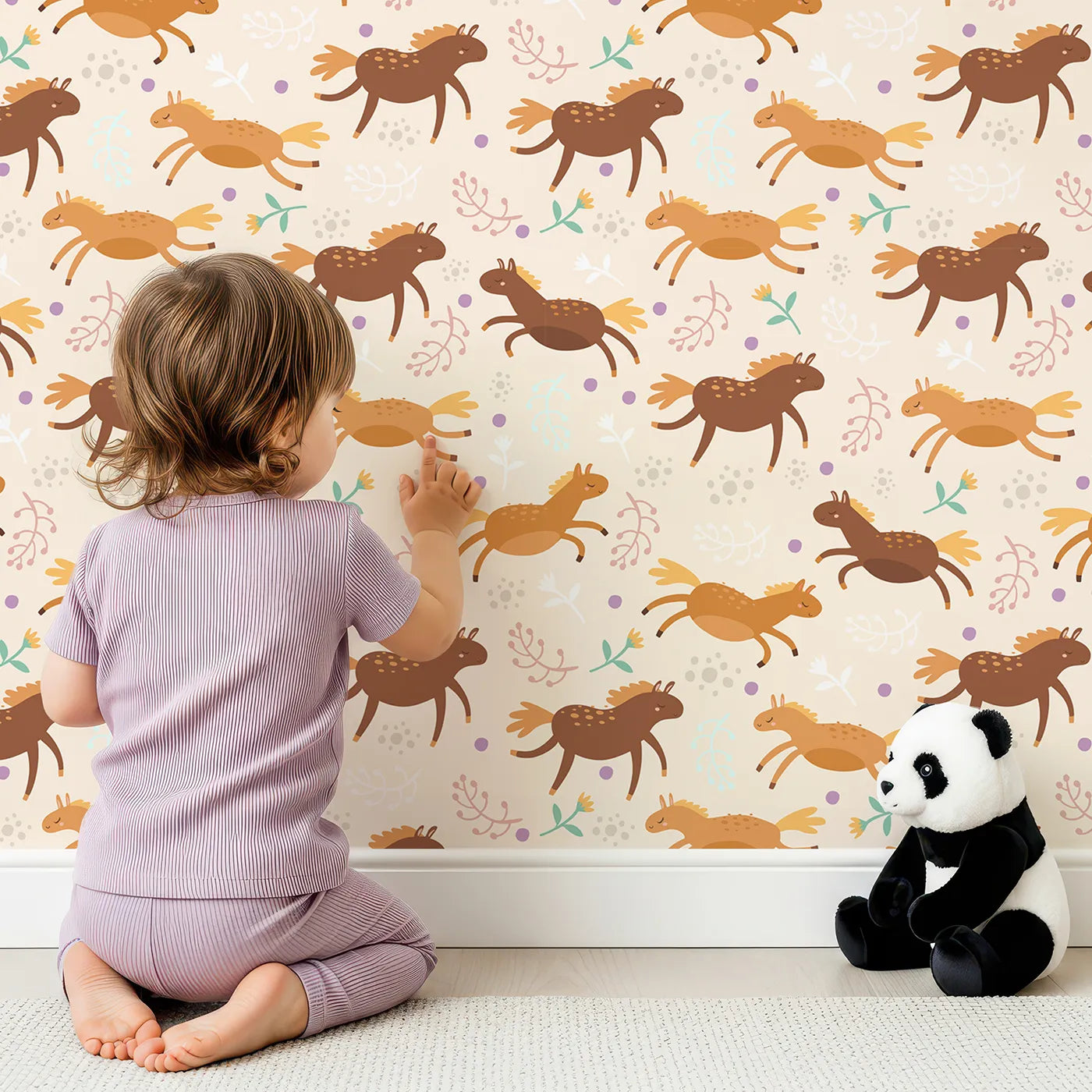 Lovely child standing in front of Whimsy Tots Dreamy Pony Meadow Wallpaper in Cream with horse, flower, leaf, dot in design.