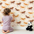 Lovely child standing in front of Whimsy Tots Dreamy Pony Meadow Wallpaper in Cream with horse, flower, leaf, dot in design. Lovely child standing in front of Whimsy Tots Dreamy Pony Meadow Wallpaper in Cream with horse, flower, leaf, dot in design.